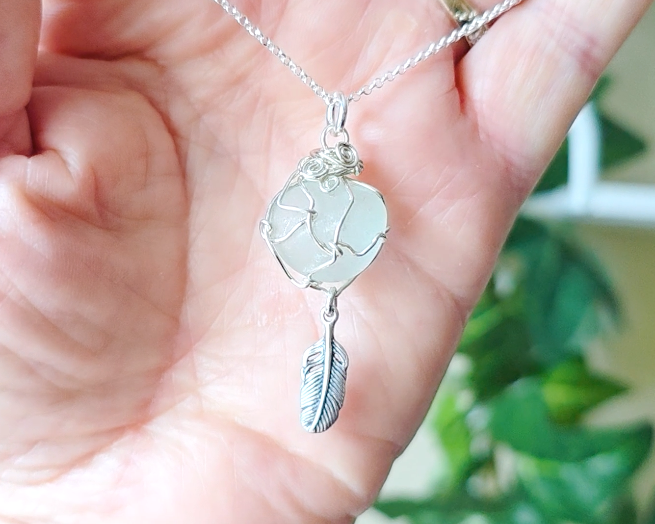 Silver Pendant with Aqua Blue Sea Glass and dangling Silver Feather on Silver Rolo chain displayed in hand