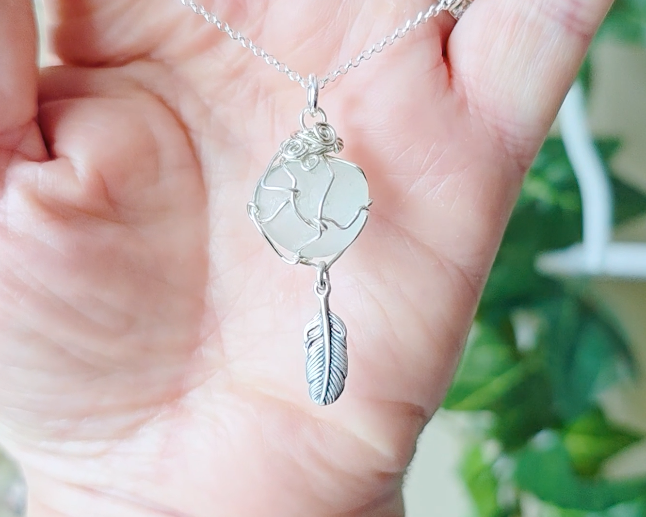 Silver Pendant with Aqua Blue Sea Glass and dangling Silver Feather on Silver Rolo chain displayed in hand
