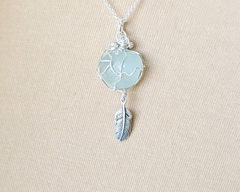 Silver Pendant with Aqua Blue Sea Glass and dangling Silver Feather on Silver Rolo chain displayed on beige