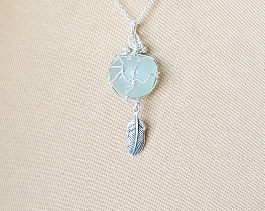 Silver Pendant with Aqua Blue Sea Glass and dangling Silver Feather on Silver Rolo chain displayed on beige