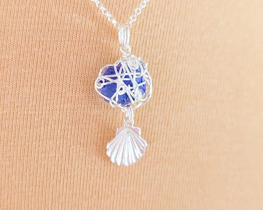 Silver Wire Wrapped Sapphire cobalt blue sea glass pendant with dangling shell on rolo chain with beige background