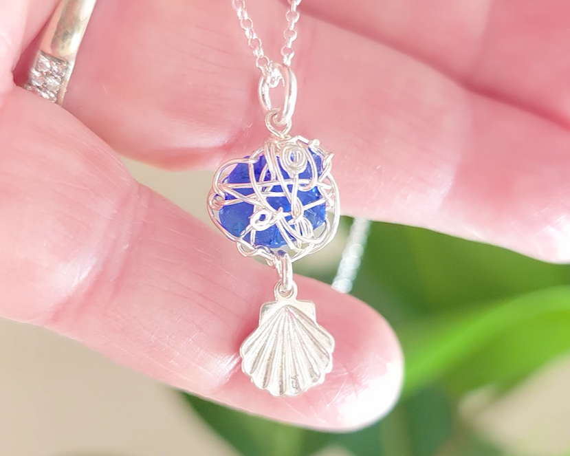 Silver Wire Wrapped Sapphire cobalt blue sea glass pendant with dangling shell on rolo chain in hand 