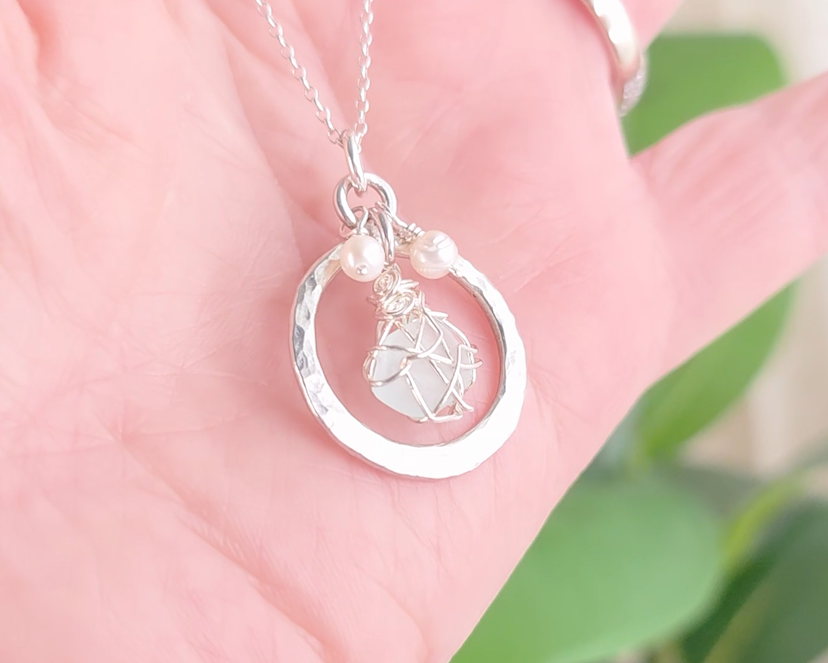 Round Circle Silver Pendant with wire wrapped Aqua Blue Beach Glass and two small white pearls on chain displayed on hand 