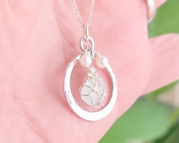 Round Circle Silver Pendant with wire wrapped Aqua Blue Beach Glass and two small white pearls on chain displayed on hand 