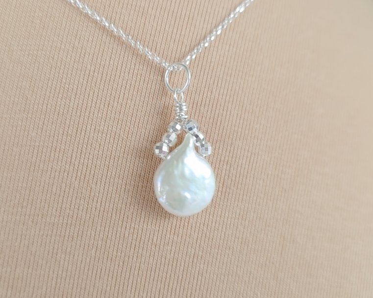 Handmade Sterling Silver Pearl Pendant with a large rounder drop shape white freshwater Cultured Pearl with sparkly silver beads wire wrapped to a round bail on silver chain with beige background 