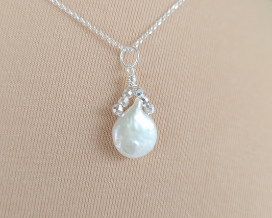 Handmade Sterling Silver Pearl Pendant with a large rounder drop shape white freshwater Cultured Pearl with sparkly silver beads wire wrapped to a round bail on silver chain with beige background 