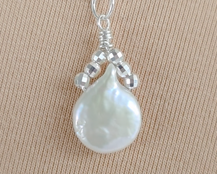 Handmade Sterling Silver Pearl Pendant with a large rounder drop shape white freshwater Cultured Pearl with sparkly silver beads wire wrapped to a round bail on silver chain with beige background 