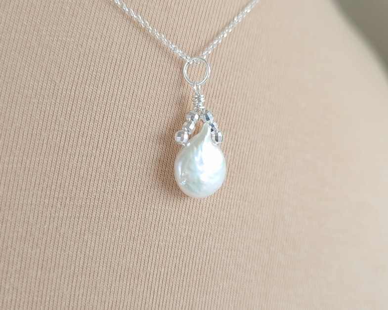Handmade Sterling Silver Pearl Pendant with a large rounder drop shape white freshwater Cultured Pearl with sparkly silver beads wire wrapped to a round bail on silver chain with beige background 