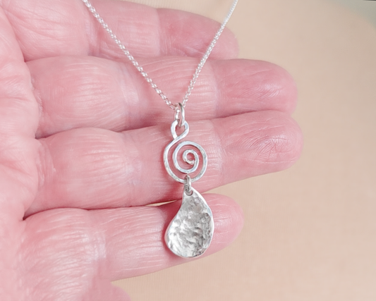 Handmade sterling silver pendant with Celtic Coil on top and drop shaped pendant dangling below on silver chain in hand