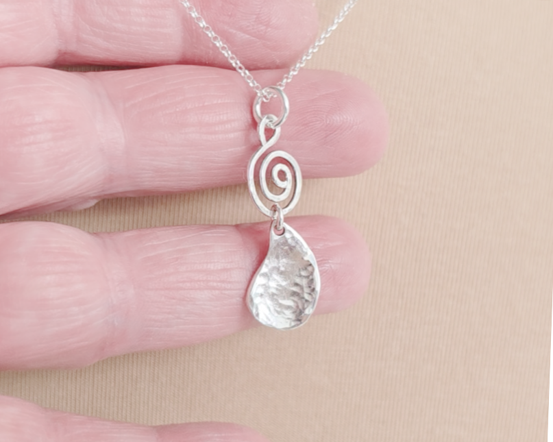Handmade sterling silver pendant with Celtic Coil on top and drop shaped pendant dangling below on silver chain in hand