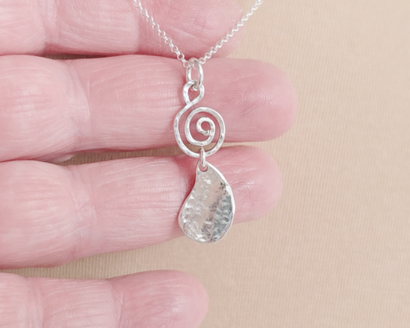 Handmade sterling silver pendant with Celtic Coil on top and drop shaped pendant dangling below on silver chain in hand