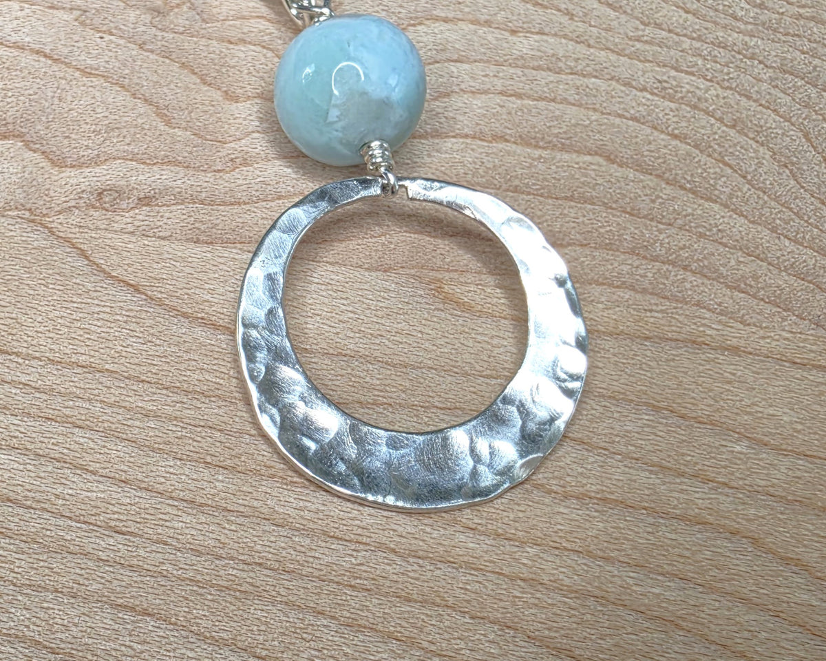 Handmade round sterling silver pendant with wire wrapped round pale blue larimar stone dangling on chain displayed on wood background 