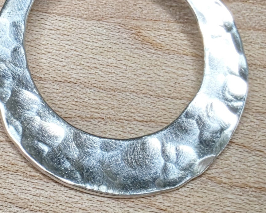Handmade round sterling silver pendant displayed on wood background 