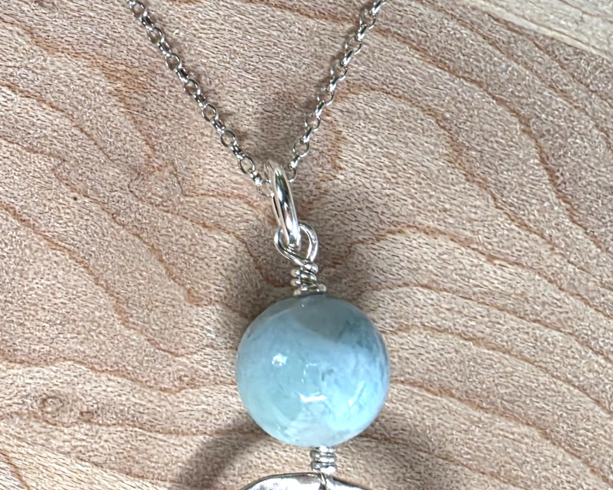 Handmade round sterling silver pendant with wire wrapped round pale blue larimar stone dangling on chain displayed on wood background 