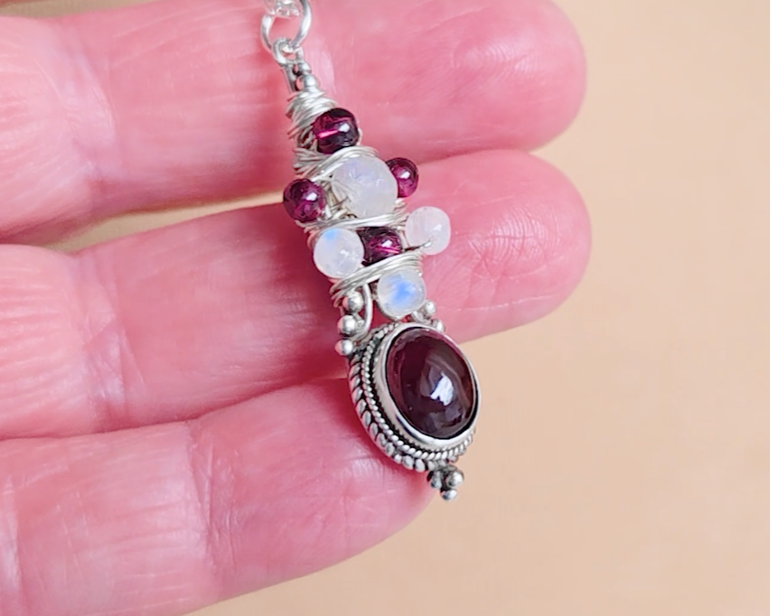 Handmade Boho style wire wrapped pendant with oval shape deep red Garnet gemstone wrapped with sterling silver wire small round garnets and faceted Moonstones in hand 