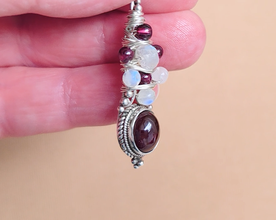 Handmade Boho style wire wrapped pendant with oval shape deep red Garnet gemstone wrapped with sterling silver wire small round garnets and faceted Moonstones in hand 