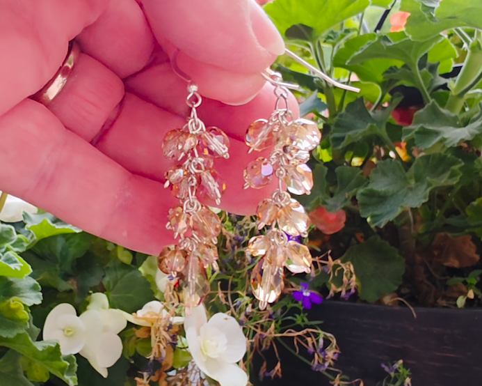 Long sparkly cluster earrings with Champagne Aurora Borealis beads on Sterling Silver with French style earring hooks in hand with Flower Garden background