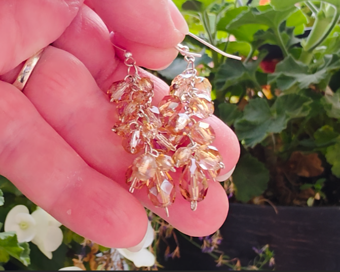 Long sparkly cluster earrings with Champagne Aurora Borealis beads on Sterling Silver with French style earring hooks in hand in garden background