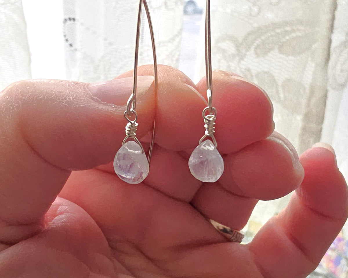 hand holding sterling silver Moonstone dangle threader style earrings with lace in background 