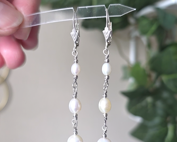 Long art deco style pearl earrings, white Freshwater Cultured Pearls, accented with fancy Sterling Silver beads on lever back earrings hooks on wood background