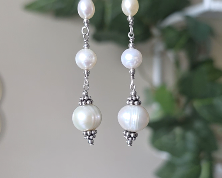 Long art deco style pearl earrings, white Freshwater Cultured Pearls, accented with fancy Sterling Silver beads on lever back earrings hooks on wood background