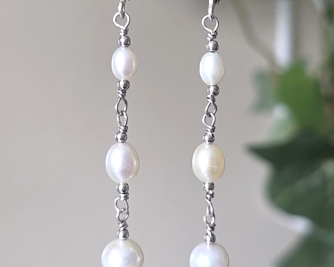 Long art deco style pearl earrings, white Freshwater Cultured Pearls, accented with fancy Sterling Silver beads on lever back earrings hooks on white background with leaves