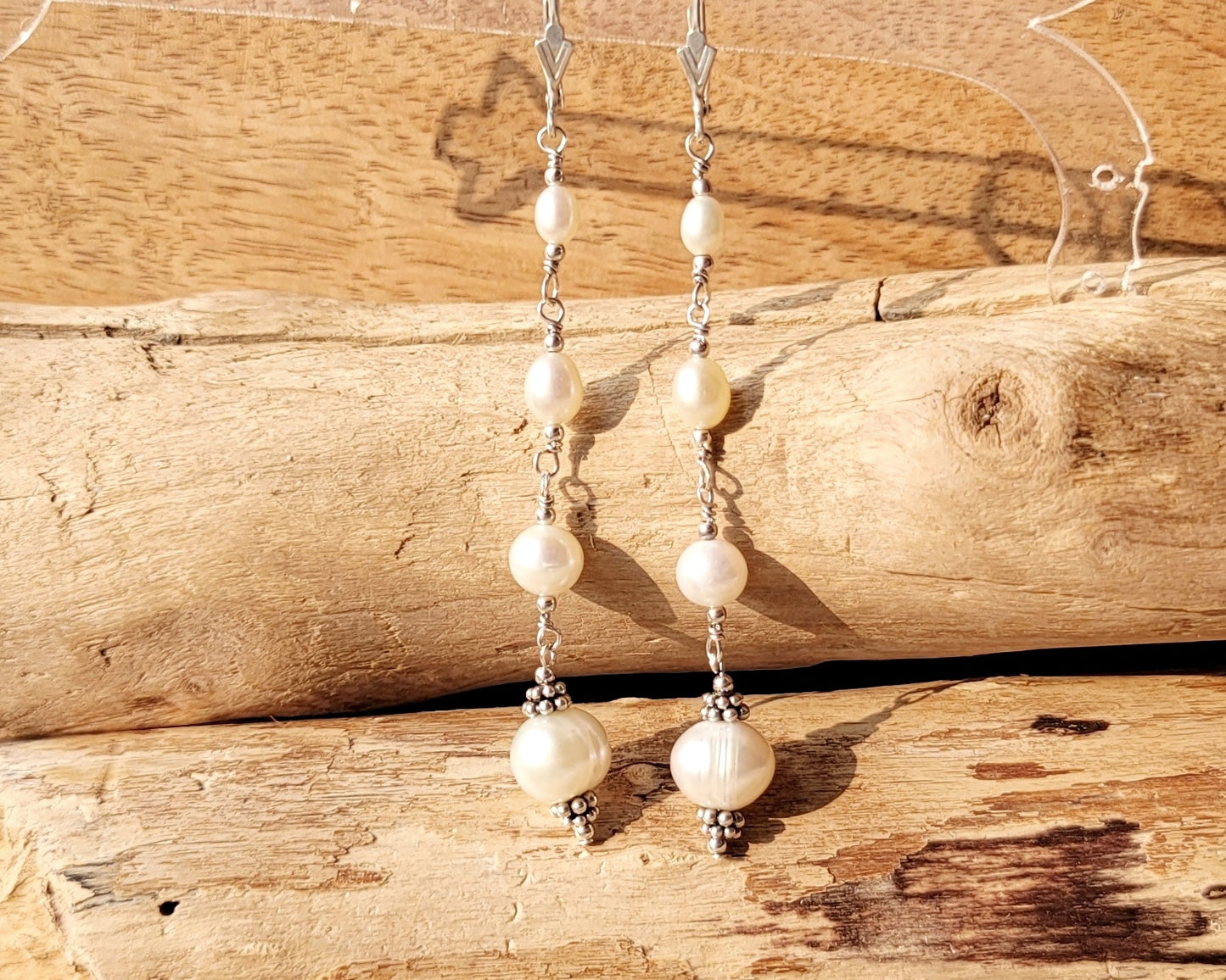 Long art deco style pearl earrings, white Freshwater Cultured Pearls, accented with fancy Sterling Silver beads on lever back earrings hooks on wood background