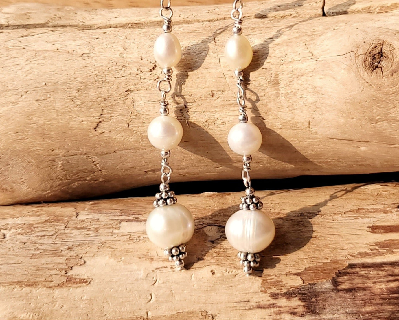 Long art deco style pearl earrings, white Freshwater Cultured Pearls, accented with fancy Sterling Silver beads on lever back earrings hooks on wood background