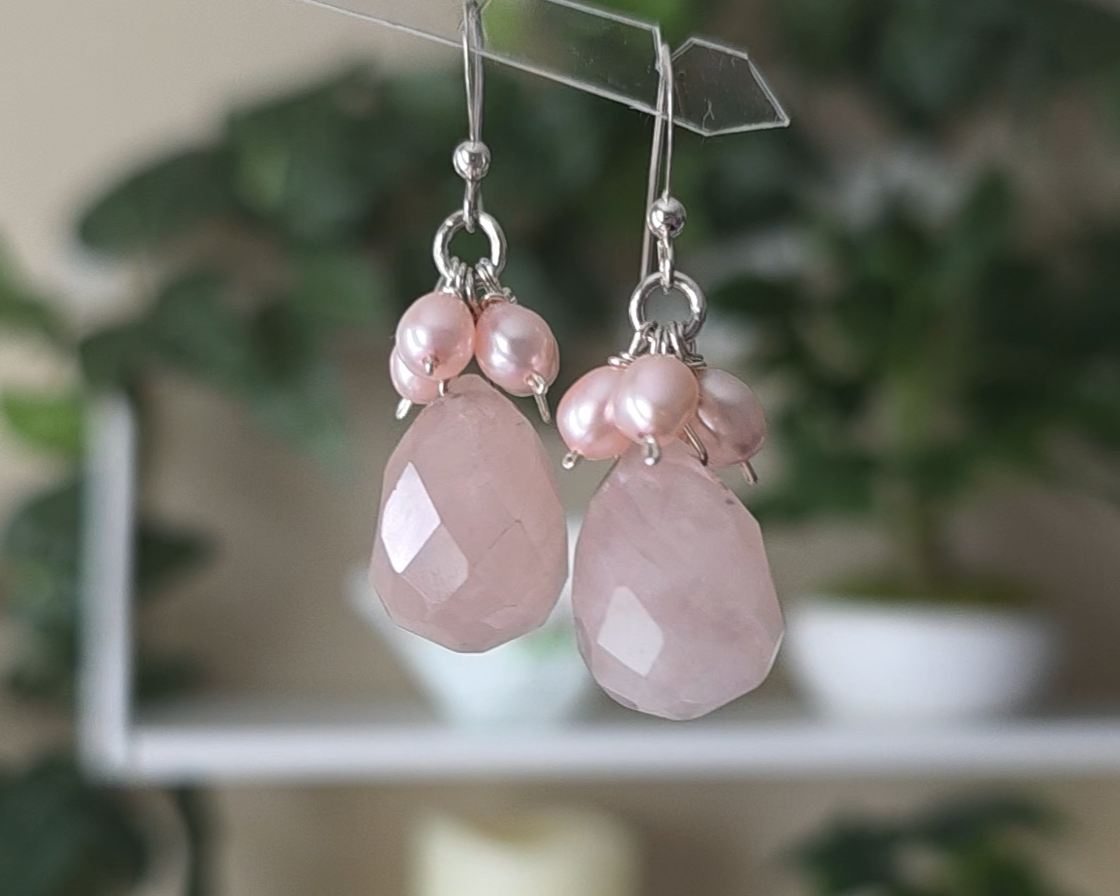 Long pink dangle earrings with large faceted Rose Quartz  sones and clusters of & pink Freshwater Cultured Pearls dangling from silver earring hooks, with plants in background 