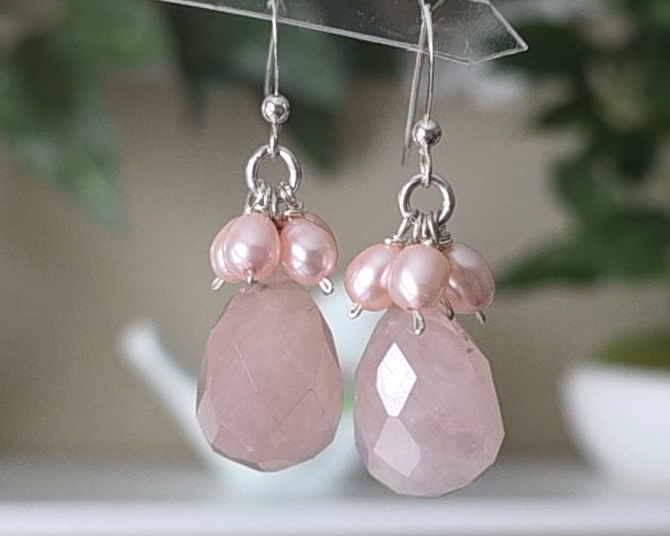 Long pink dangle earrings with large faceted Rose Quartz  sones and clusters of & pink Freshwater Cultured Pearls dangling from silver earring hooks, with plants in background 