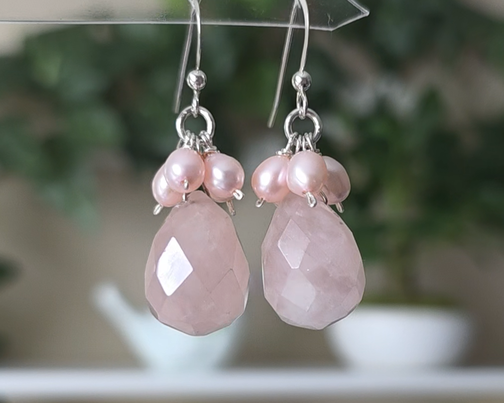 Long pink dangle earrings with large faceted Rose Quartz  sones and clusters of & pink Freshwater Cultured Pearls dangling from silver earring hooks, with plants in background 