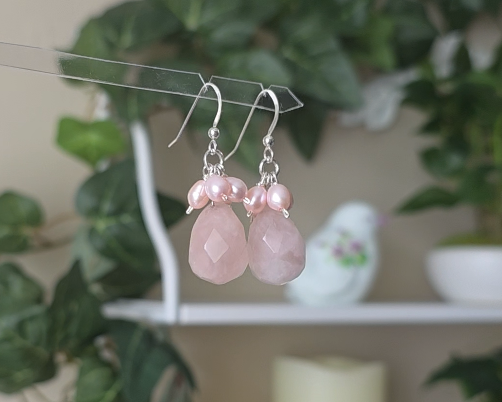 Long pink dangle earrings with large faceted Rose Quartz  sones and clusters of & pink Freshwater Cultured Pearls dangling from silver earring hooks, with plants in background 