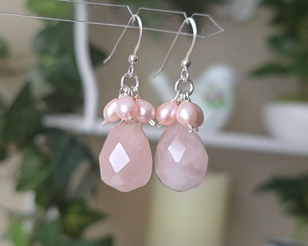 Long pink dangle earrings with large faceted Rose Quartz  sones and clusters of & pink Freshwater Cultured Pearls dangling from silver earring hooks, with plants in background 