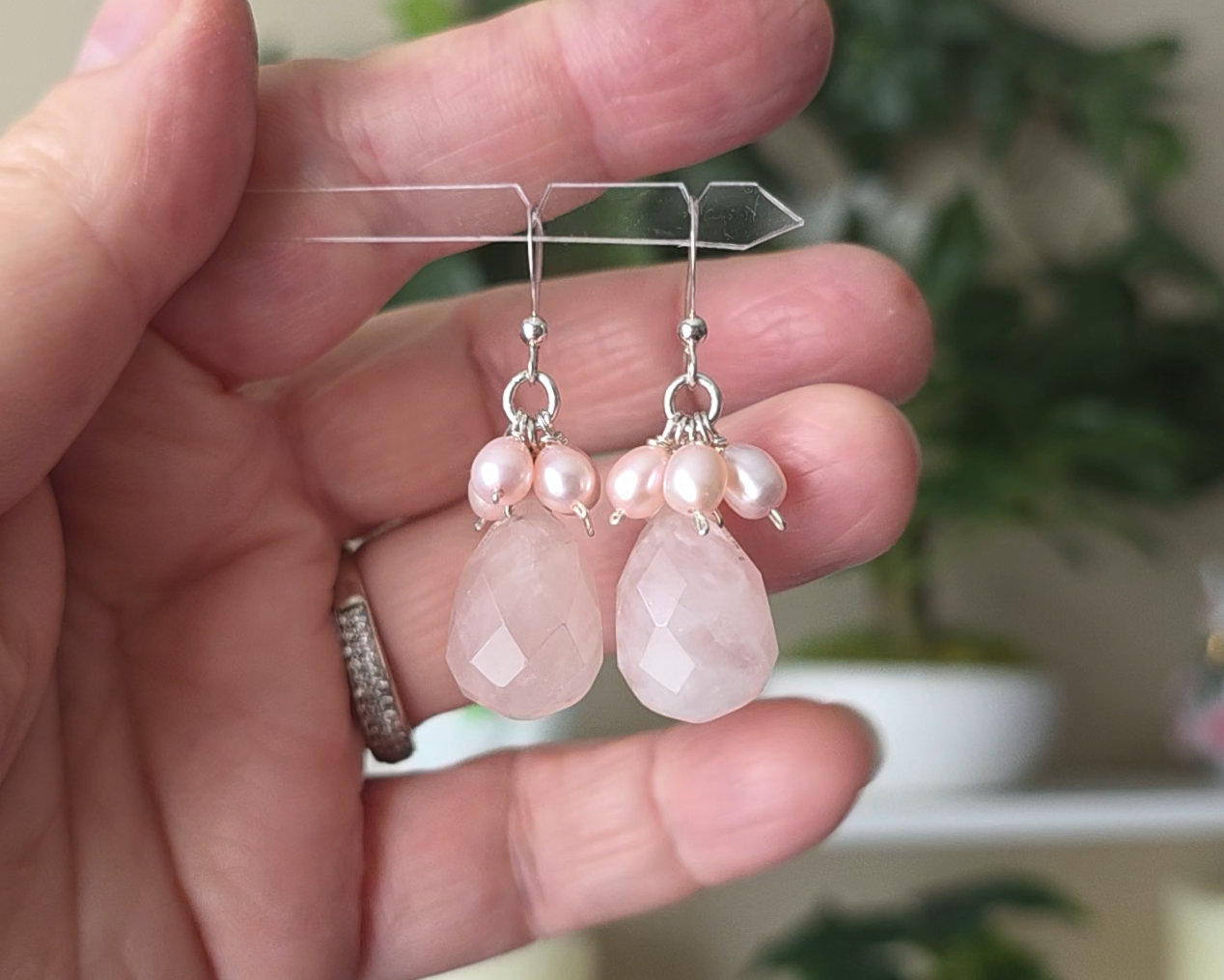 Long pink dangle earrings with large faceted Rose Quartz  sones and clusters of & pink Freshwater Cultured Pearls dangling from silver earring hooks, with plants in background 