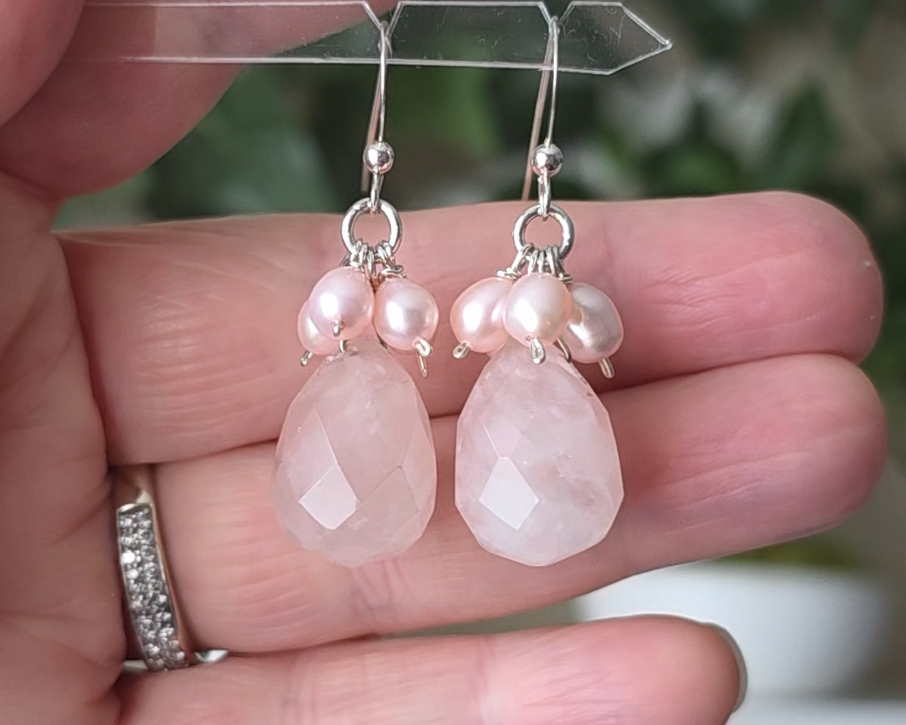 Long pink dangle earrings with large faceted Rose Quartz  sones and clusters of & pink Freshwater Cultured Pearls dangling from silver earring hooks, with plants in background 