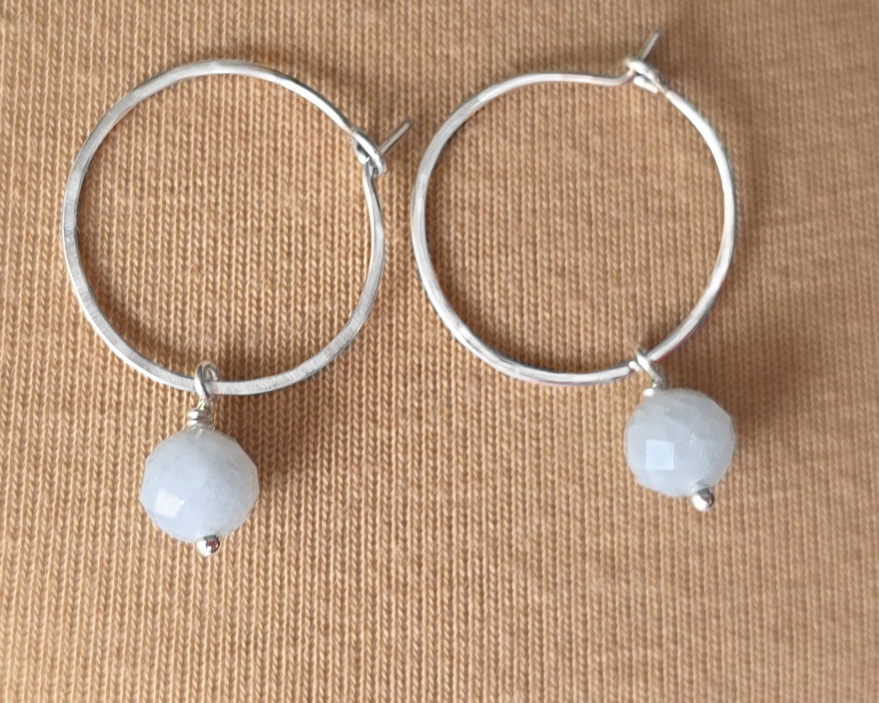 Sterling Silver hoop earrings with pale blue aquamarine dangles, on beige background 