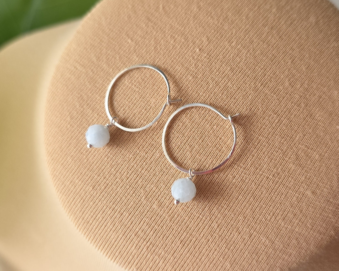 Sterling Silver hoop earrings with pale blue aquamarine dangles, on beige background 