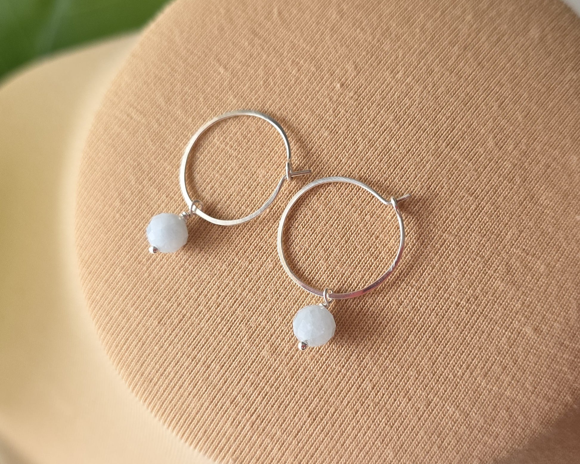 Sterling Silver hoop earrings with pale blue aquamarine dangles, on beige background 