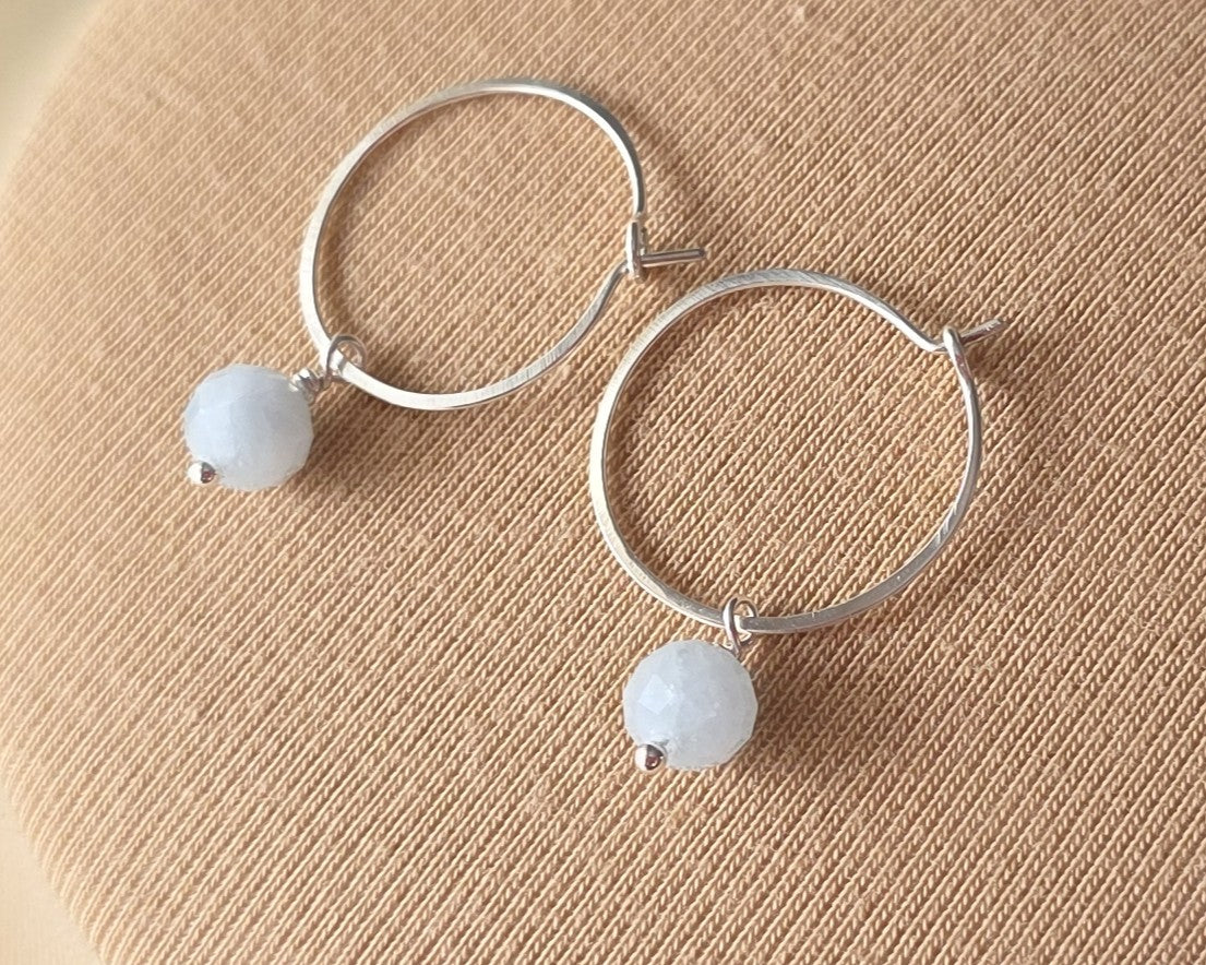Sterling Silver hoop earrings with pale blue aquamarine dangles, on beige background 