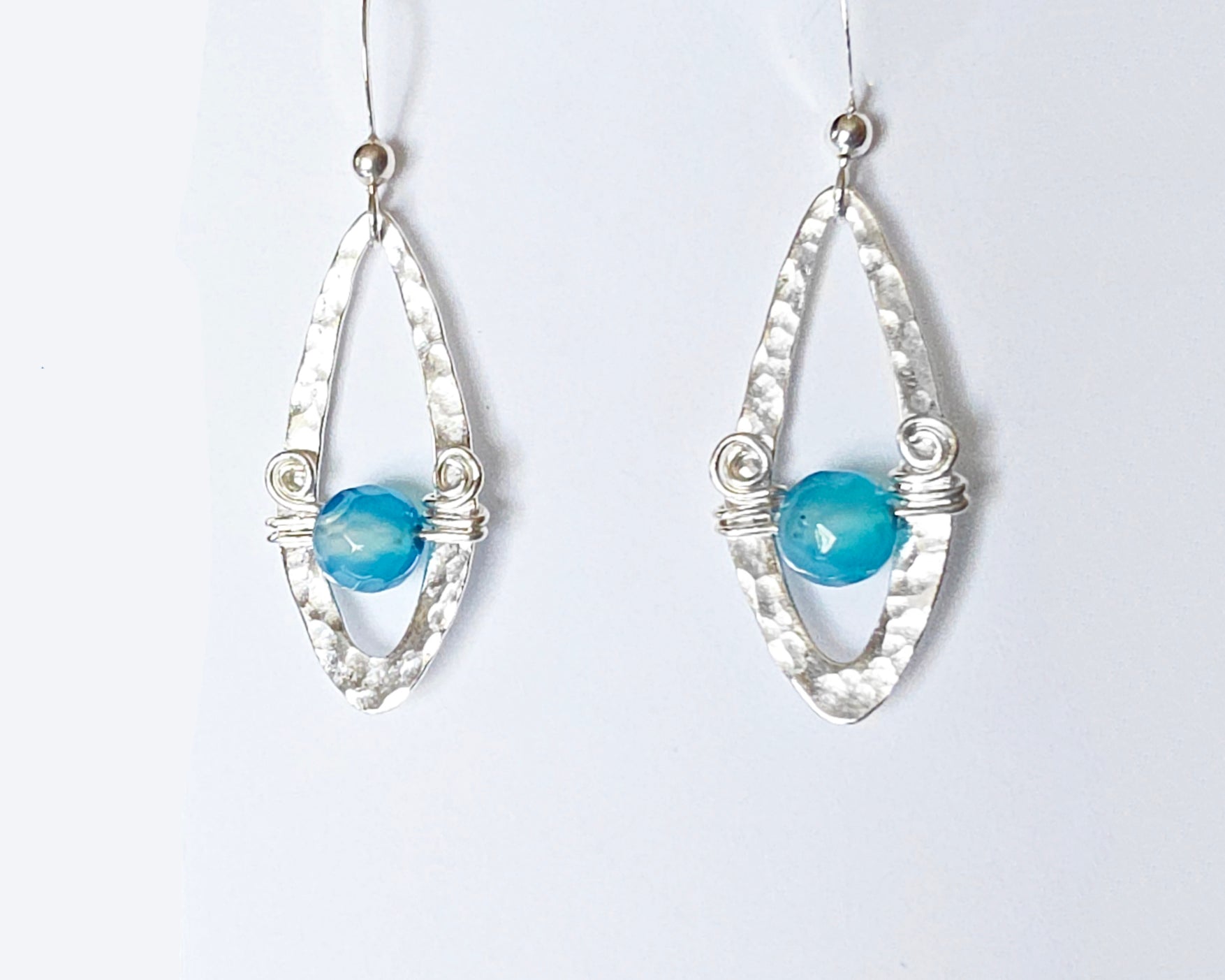 Long Sterling Silver Earrings with Blue Banded Agate stones and Celtic Eternity Coil designs on a wing like hammered design on French style earring hooks, on white background 