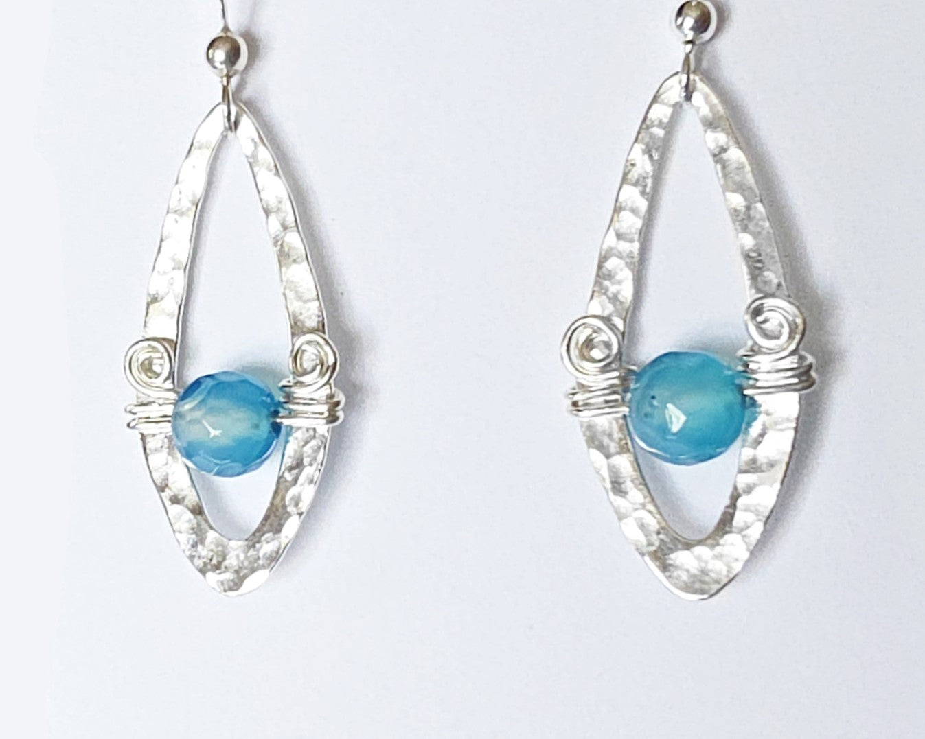 Long Sterling Silver Earrings with Blue Banded Agate stones and Celtic Eternity Coil designs on a wing like hammered design on French style earring hooks, on white background 