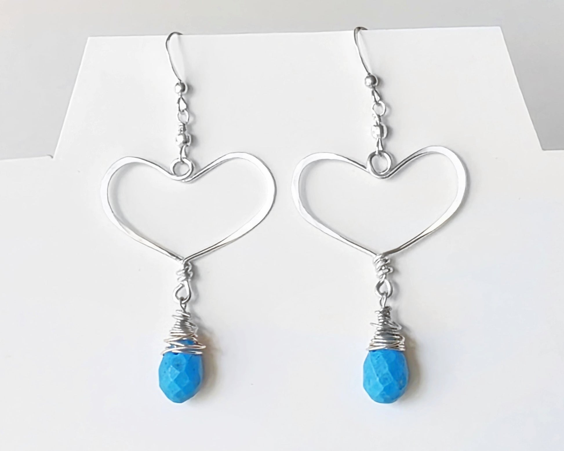 Long Sterling Silver Heart Dangle Earrings with large Hoop like Hearts and dangling Howlite drop shape stone, dangling from French style earring hooks, displayed on white background.