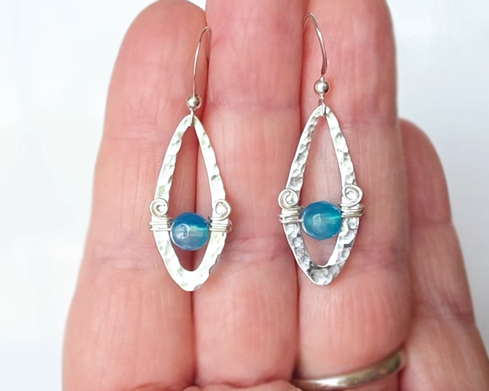 Long Sterling Silver Earrings with Blue Banded Agate stones and Celtic Eternity Coil designs on a wing like hammered design on French style earring hooks, displayed on hand 