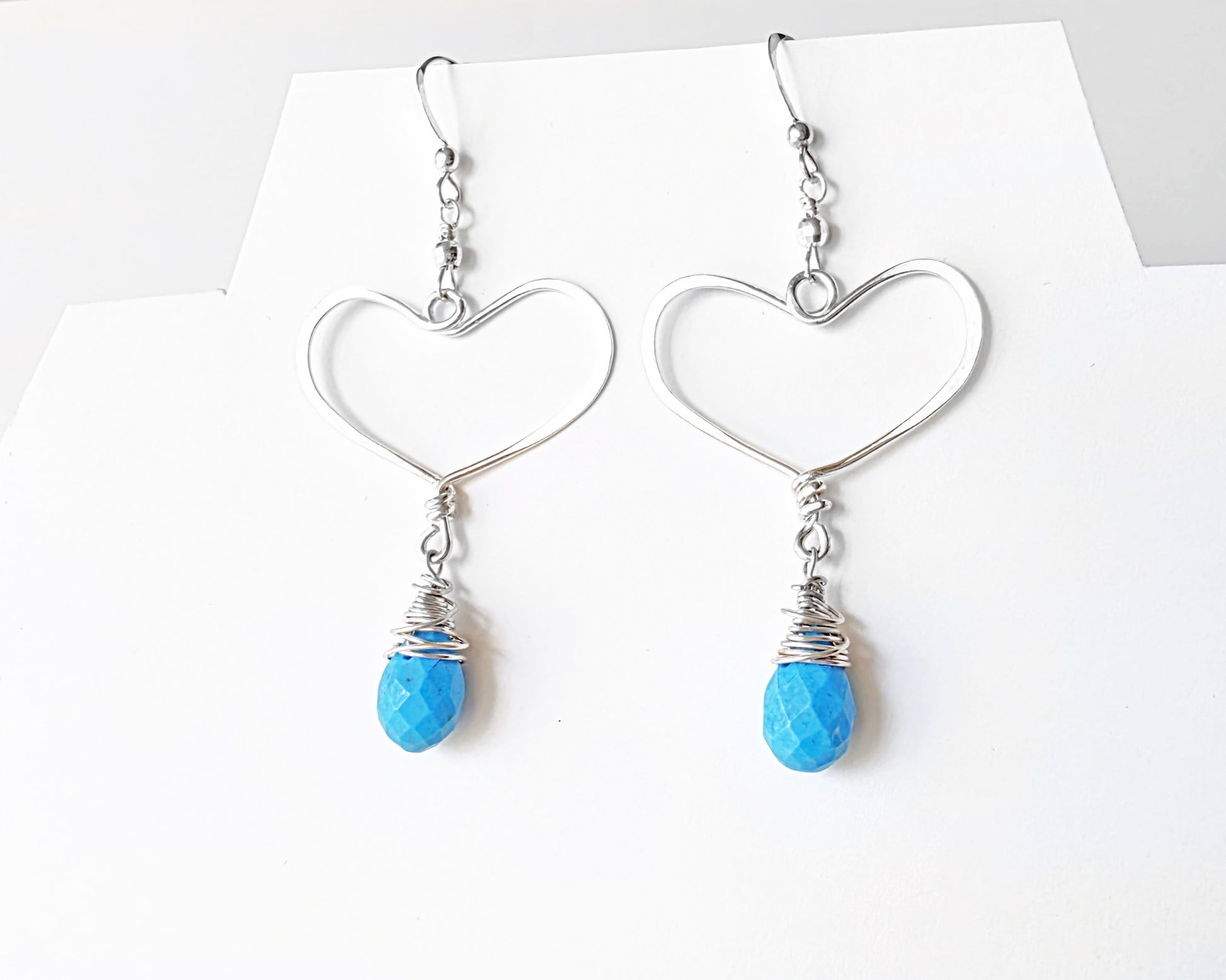 Long Sterling Silver Heart Dangle Earrings with large Hoop like Hearts and dangling Howlite drop shape stone, dangling from French style earring hooks, displayed on white background.