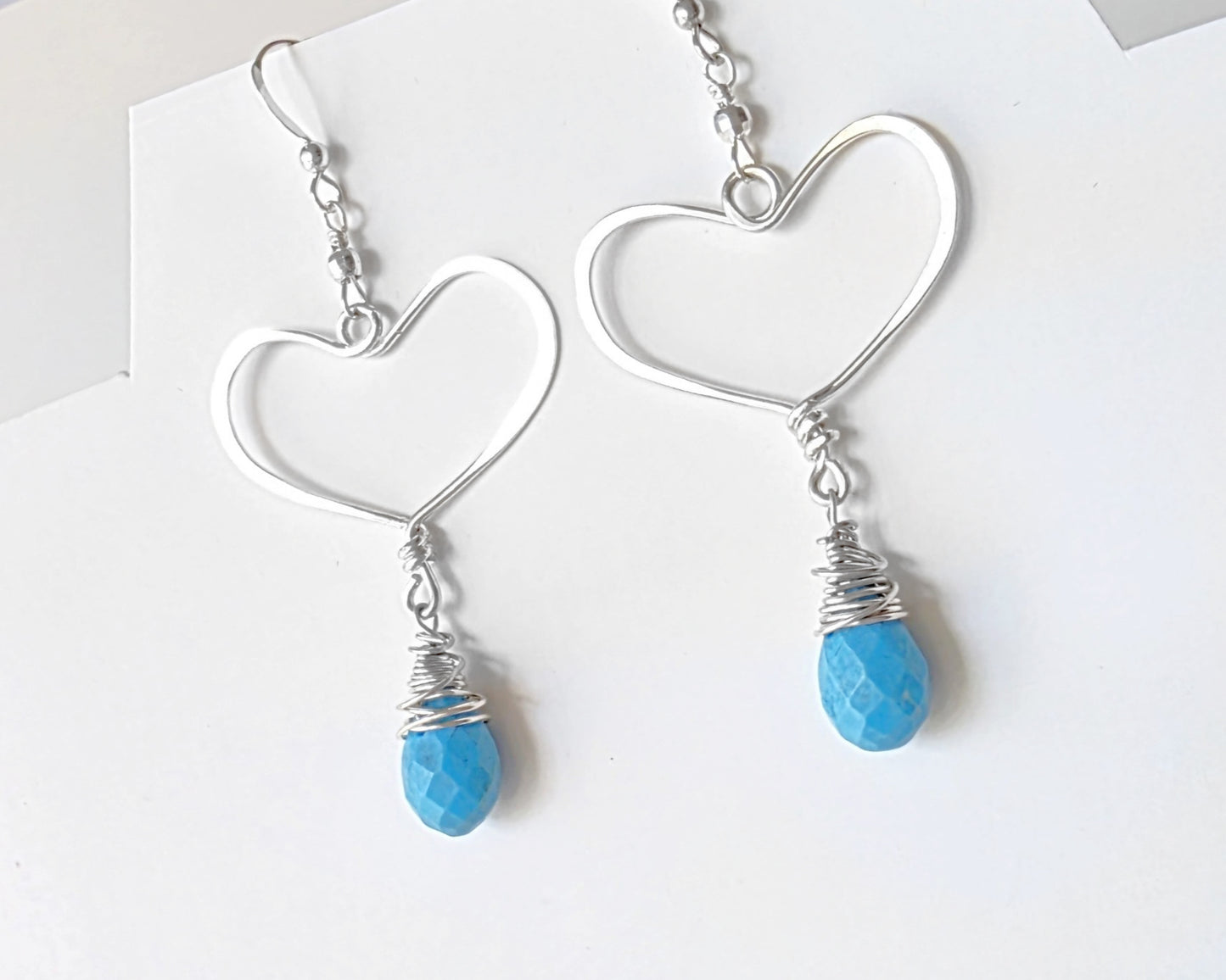 Long Sterling Silver Heart Dangle Earrings with large Hoop like Hearts and dangling Howlite drop shape stone, dangling from French style earring hooks, displayed on white background.