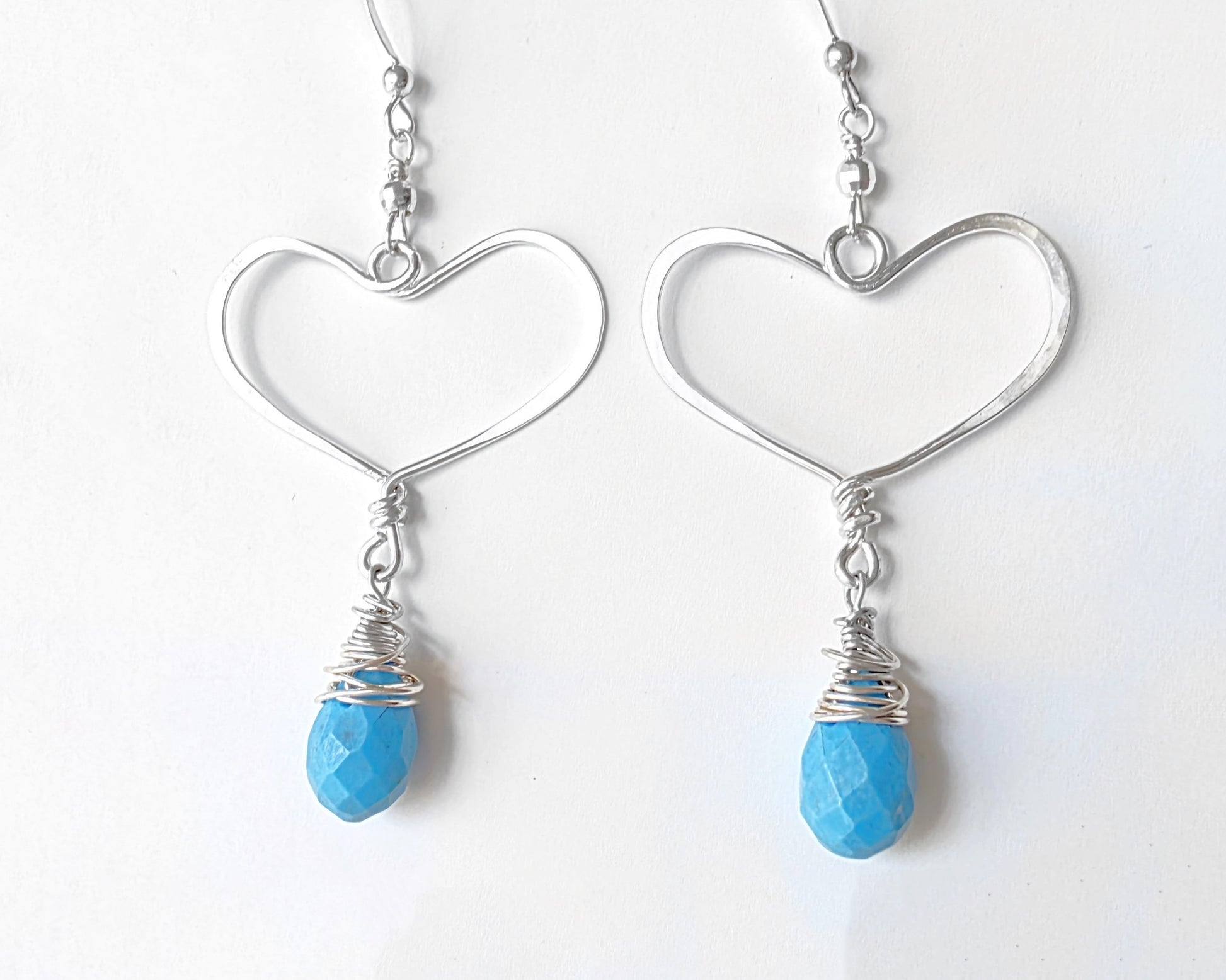 Long Sterling Silver Heart Dangle Earrings with large Hoop like Hearts and dangling Howlite drop shape stone, dangling from French style earring hooks, displayed on white background.