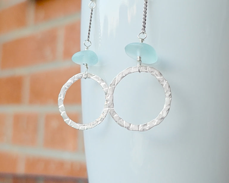Long hoop dangle earrings on chain with aqua blue sea glass, with French hooks, displayed on white and brick. 