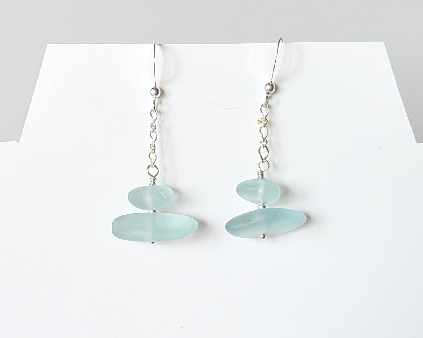 A pair of Long handmade Sterling Silver Pale Aqua blue Sea glass earrings with blue satin glass on long chain with french style earring hooks on white background