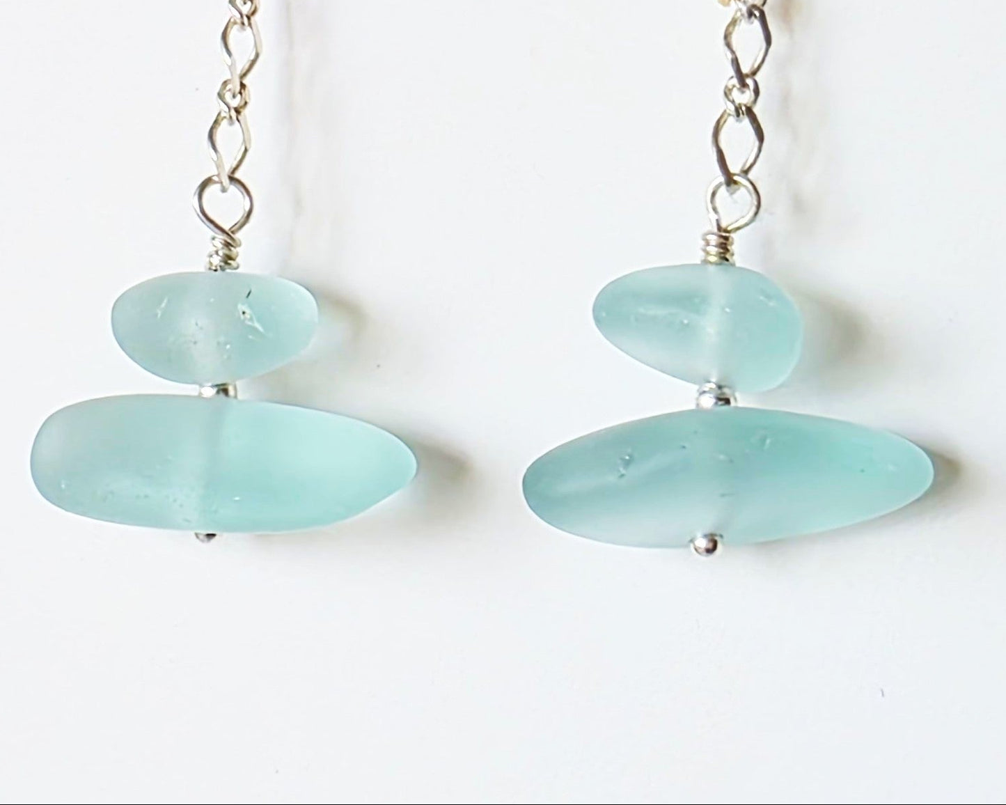 A pair of Long handmade Sterling Silver Pale Aqua blue Sea glass earrings with blue satin glass on long chain with french style earring hooks on white background