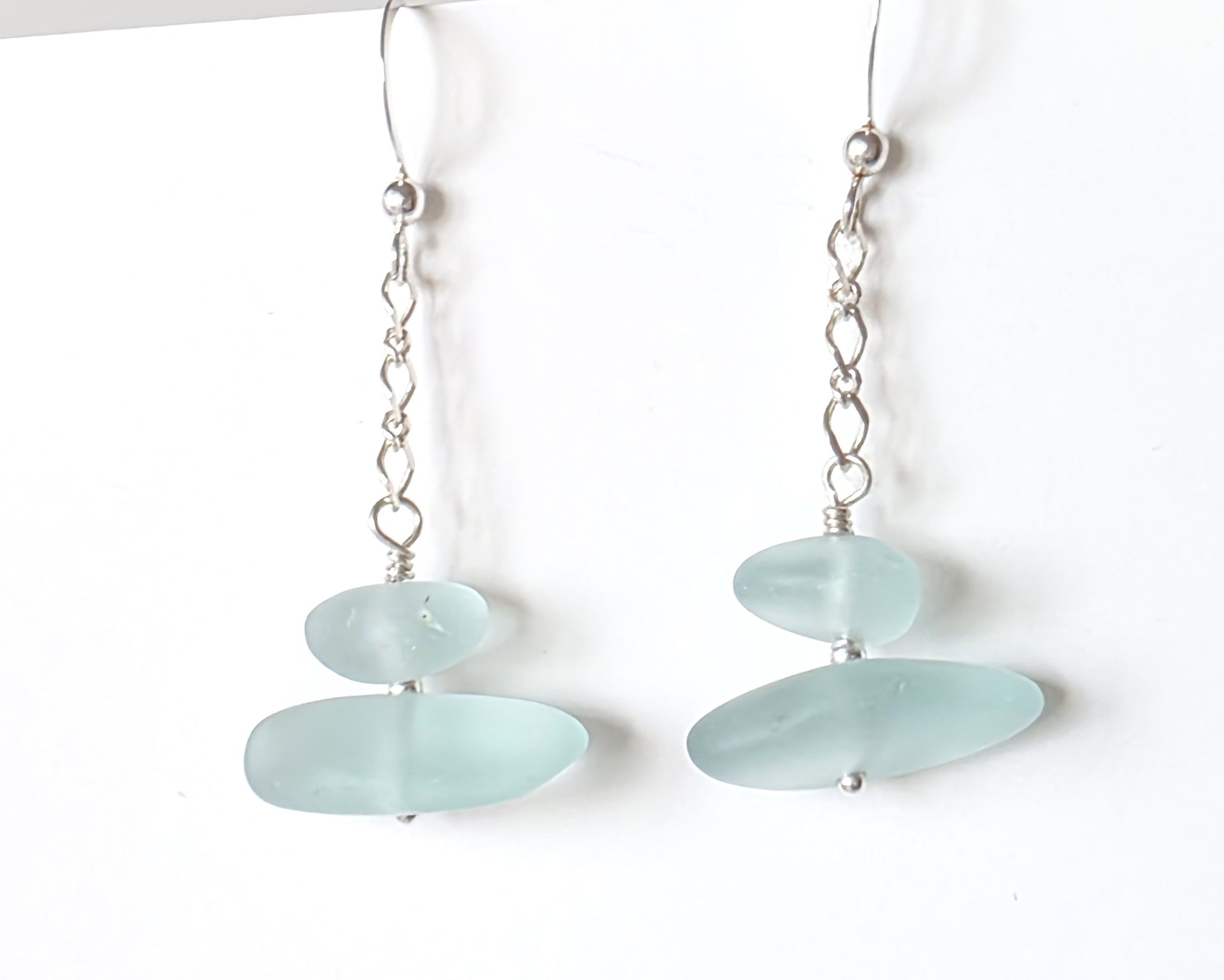 A pair of Long handmade Sterling Silver Pale Aqua blue Sea glass earrings with blue satin glass on long chain with french style earring hooks on white background